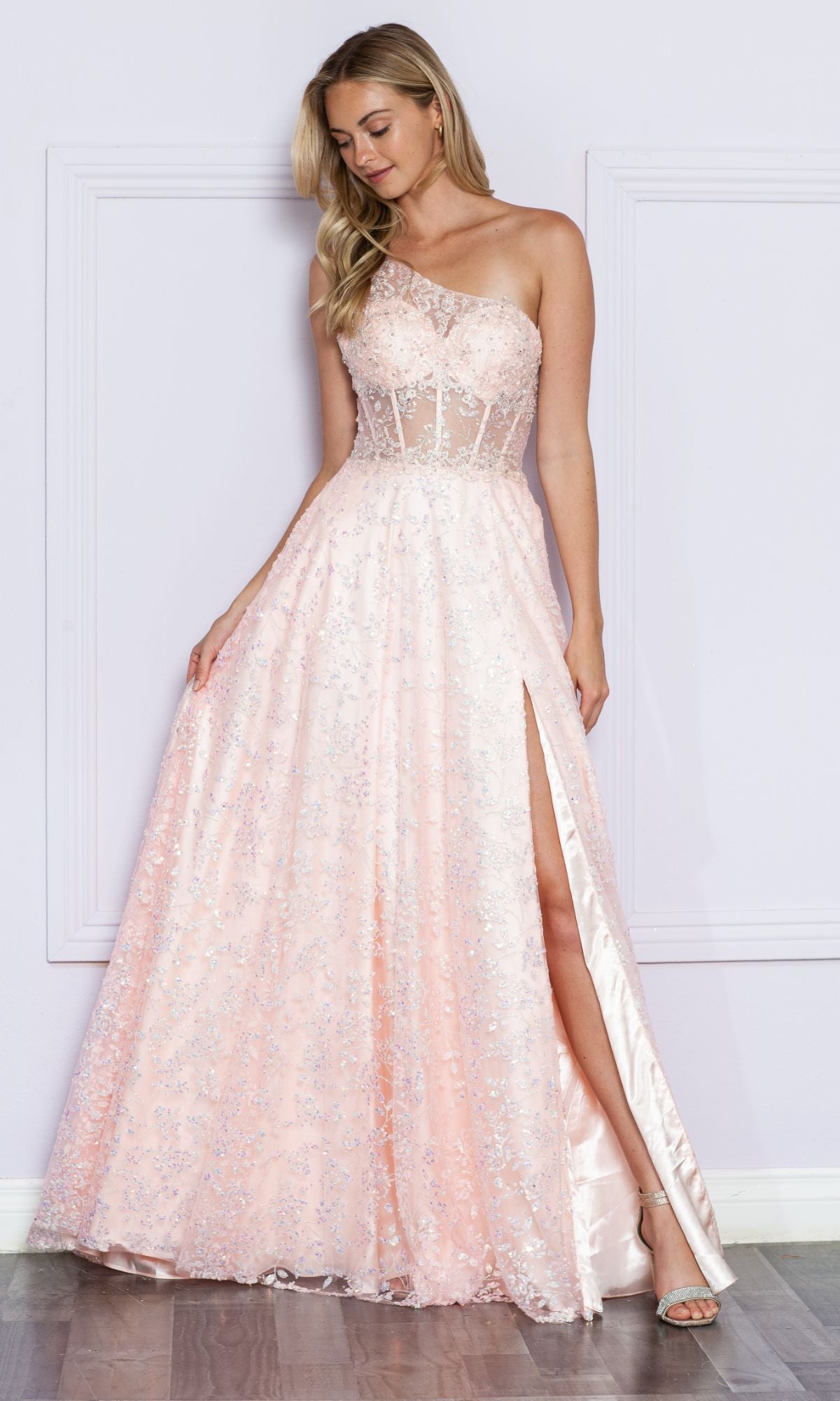 A woman in the One-Shoulder Embroidered Long Prom Dress 9372 in peach, featuring silver embellishments and a high slit, stands against a light purple wall.